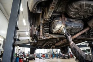 Käytetyn hatchbackin pohjaa ja polttoainetankin kiinnityksiä tarkastetaan nostimella taskulampun valossa