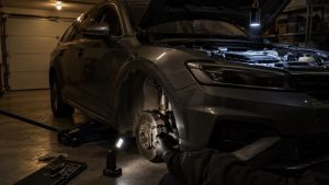 Työvalo seisoo autotallin lattialla pyöränkaaren vieressä, ja toinen työvalo roikkuu konepellin reunasta