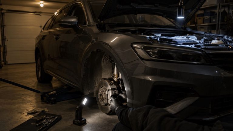 Työvalo seisoo autotallin lattialla pyöränkaaren vieressä, ja toinen työvalo roikkuu konepellin reunasta